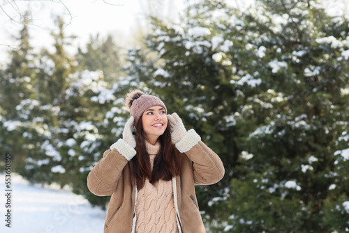 Beautiful smiling woman wearing warm clothes and walking in snowy winter forest