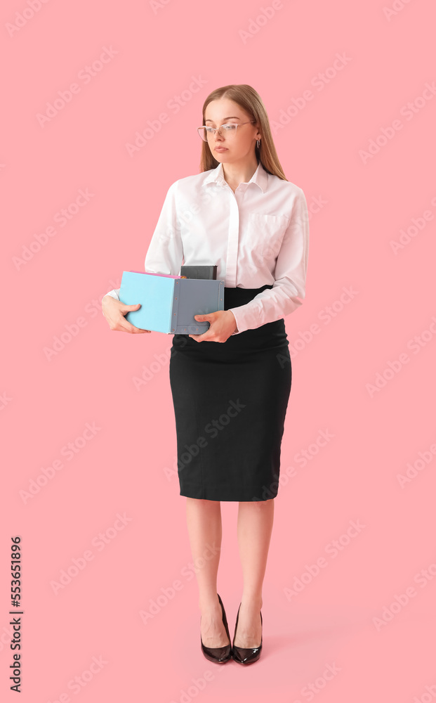Fired young woman holding box with office stuff on pink background Fired young woman holding box with office stuff on pink background