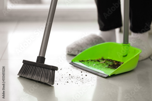 Woman sweeping tile floor with broom and dustpan, closeup photo