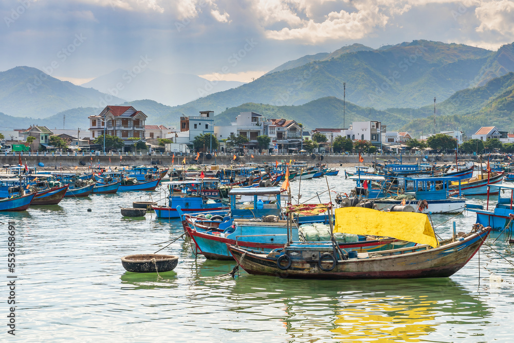 Colourful fishing boats in a small harbour in front of a mountain range at Vihn Luong Fishing Village in Vietnam