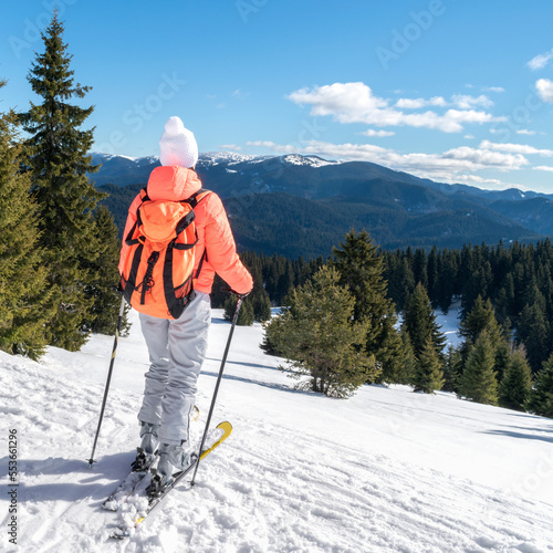 Woman ski tourist enjoy view of winter mountain forest valley during ski trip on snow slope. Ski resort Pamporovo, Bulgaria. Back view young girl skier with backpack and winter nature background photo