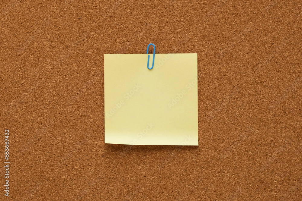 Yellow note paper with a clip on a corkboard. Blank sticker for notes with place for your text Yellow note paper with a clip on a corkboard. Blank sticker for notes with place for your text
