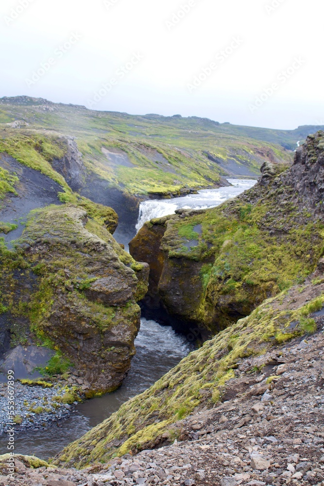 Majestic Icelandic Water fall with green moss and Lava rocks between cliff formation. damp fresh icelandic landscape with strong green and earth tones
