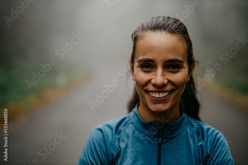 Fototapeta Naklejka Na Ścianę i Meble -  Portrait of a smiling confident female personal trainer who is standing with arms crossed in a sports outfit during the morning jogging in the forest.