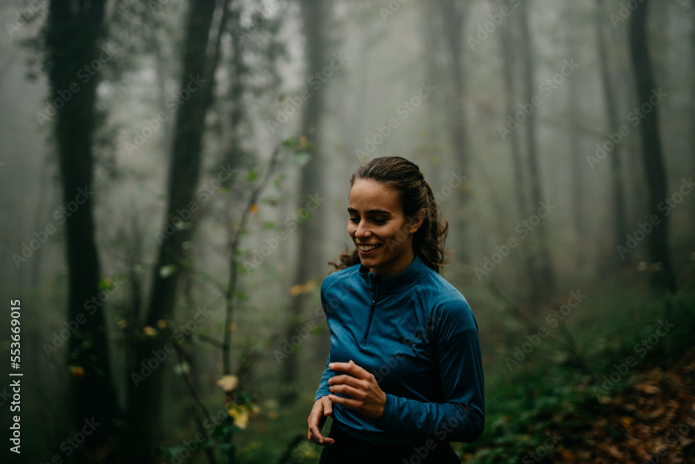 Focused and determined female have a sports recreation in the foggy forest. Smiling female jogging on a cold day Focused and determined female have a sports recreation in the foggy forest. Smiling female jogging on a cold day