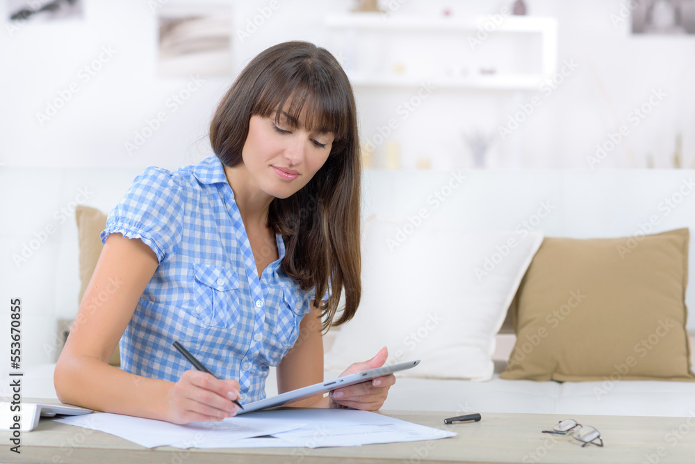 woman using tablet while doing paperwork at home woman using tablet while doing paperwork at home