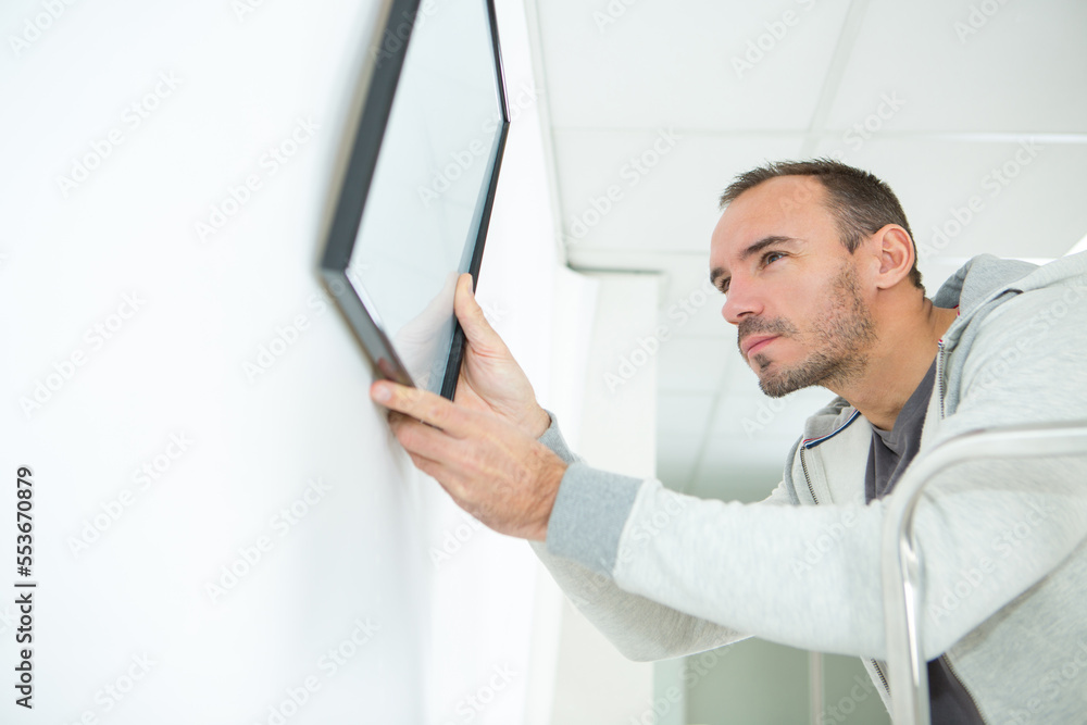 Fototapeta premium man hanging picture frames on wall at home
