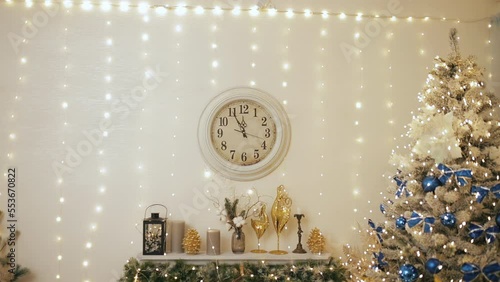 Christmas and New Year 2023 in Ukraine. Decorated fir-tree with blue bulbs and golden yellow bows. Fireplace, golden reindeer toys and clock on wall