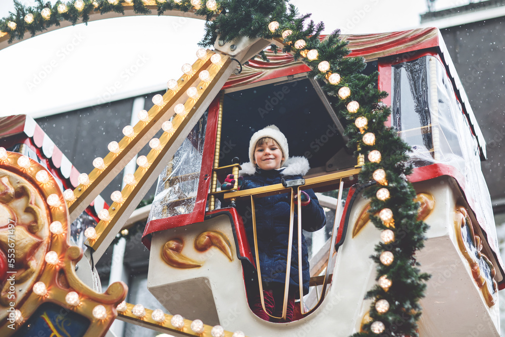 Obraz premium Happy cute preschool girl riding on ferris wheel carousel horse at Christmas funfair or market, outdoors. Little toddler child having fun on traditional family xmas market in Germany