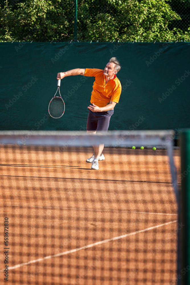 An adult man plays tennis on a sand court on a sunny day. Energy and movement. Vertical.