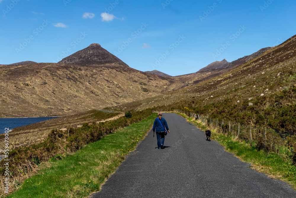Silent Valley County Down Northern Ireland - May 16 2018. Woman in a blue jacket walking her pet black dog on a path beside Silent Valley Resevoir