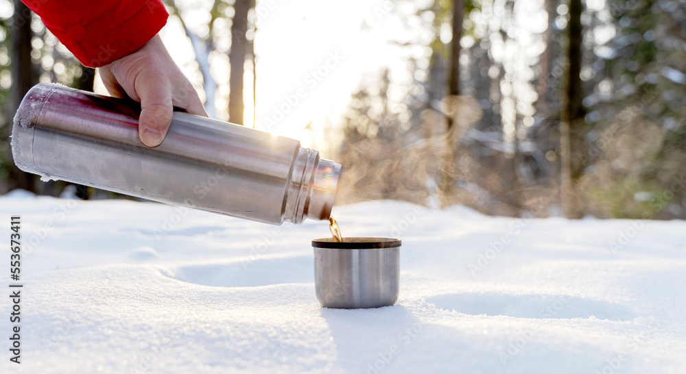 Small thermos with steaming hot drink on snow Stock Photo by