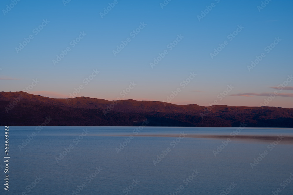 山が朝焼けに赤く染まる夜明けの湖の風景。