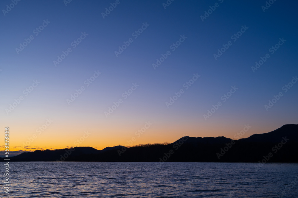 夜明けの空は美しいグラデーションに山のシルエットが際立つ湖の風景。