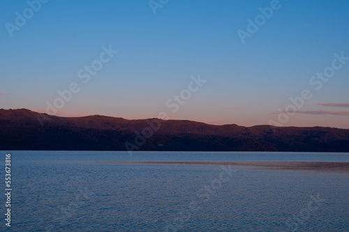 山が朝焼けに赤く染まる夜明けの湖の風景。