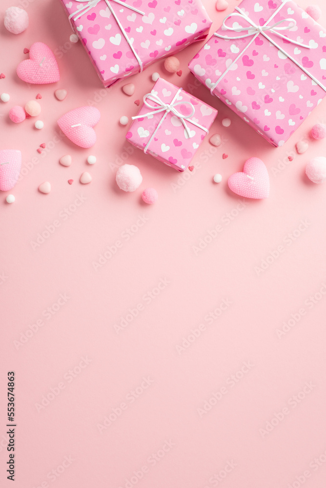 Valentine's Day concept. Top view vertical photo of present boxes in wrapping paper with heart pattern candles fluffy pompons and sprinkles on isolated pastel pink background with copyspace