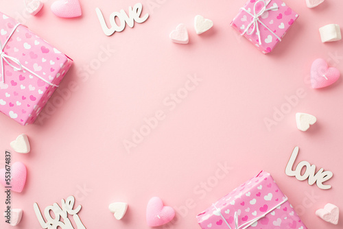 Valentine's Day concept. Top view photo of gift boxes heart shaped marshmallow inscriptions love and candles on isolated pastel pink background with empty space in the middle © ActionGP
