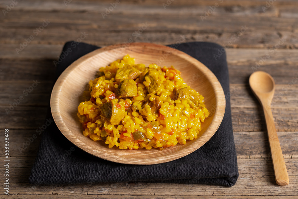 Rustic wooden plate with a portion of meat paella, on old wooden background, close-up. Rustic wooden plate with a portion of meat paella, on old wooden background, close-up.