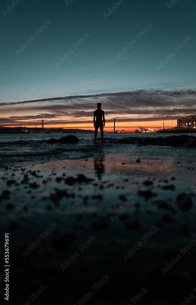 Silhouette of a young man watching the 25th of April Bridge sunset in Lisbon, Portugal