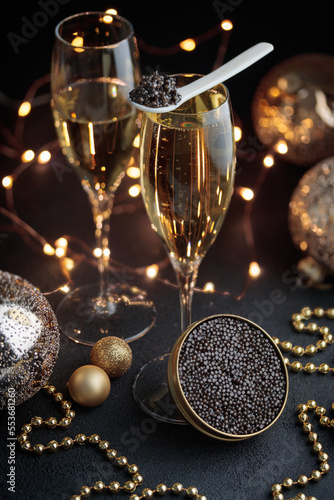 Black caviar in a mother-of-pearl spoon and jar and glass of champagne with Christmas decoration