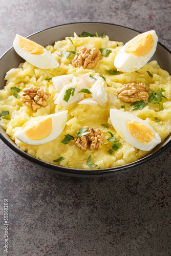 Spanish cuisine mashed potatoes with cod and garlic served with walnuts and boiled eggs close-up in a bowl on the table. Vertical