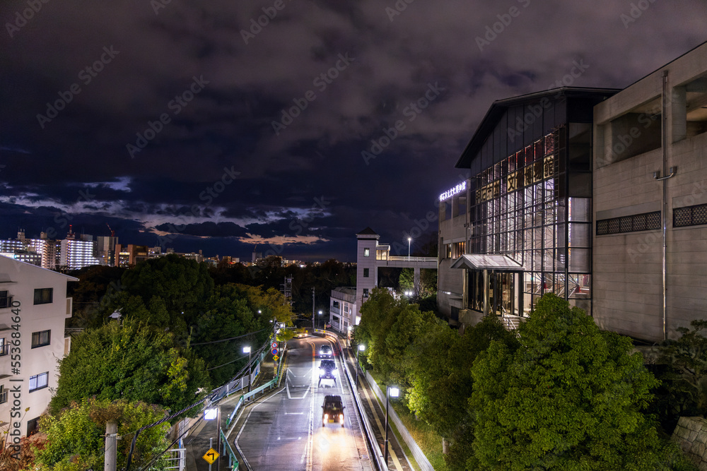 Light traffic on tree-lined road through tall buildings after sunset