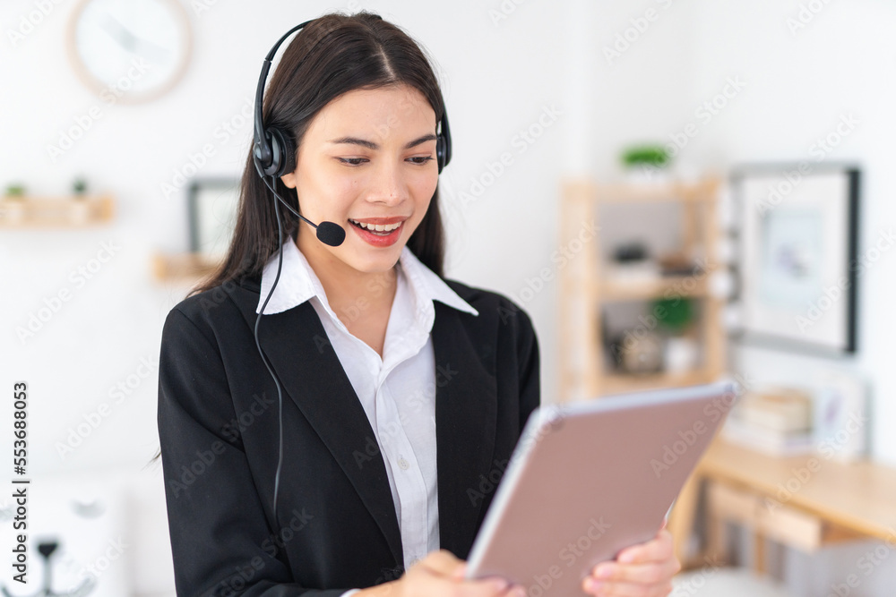 Young beautiful smart asian lady businesswoman working on digital tablet and providing customer support assistance over her wired microphone headset in an office Young beautiful smart asian lady businesswoman working on digital tablet and providing customer support assistance over her wired microphone headset in an office