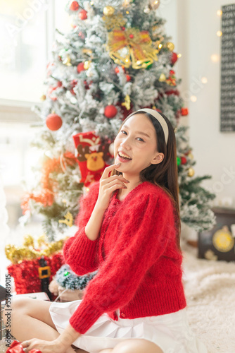 Young beautiful friendly asian female lady with red long sleeve sweater shirt and cute headband posing different look cheerfully with a nicely decorated Christmas tree in a room © asean studio