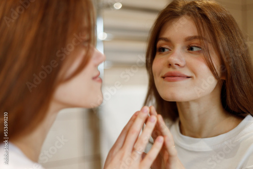 Positive woman in the morning looks at the reflection in the mirror  facial skin care.