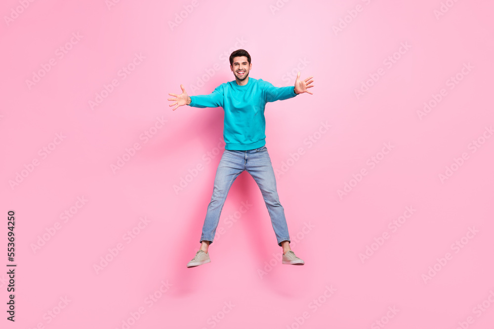 Full length photo of attractive young man jumping stretching hands hug excited dressed stylish blue look isolated on pink color background