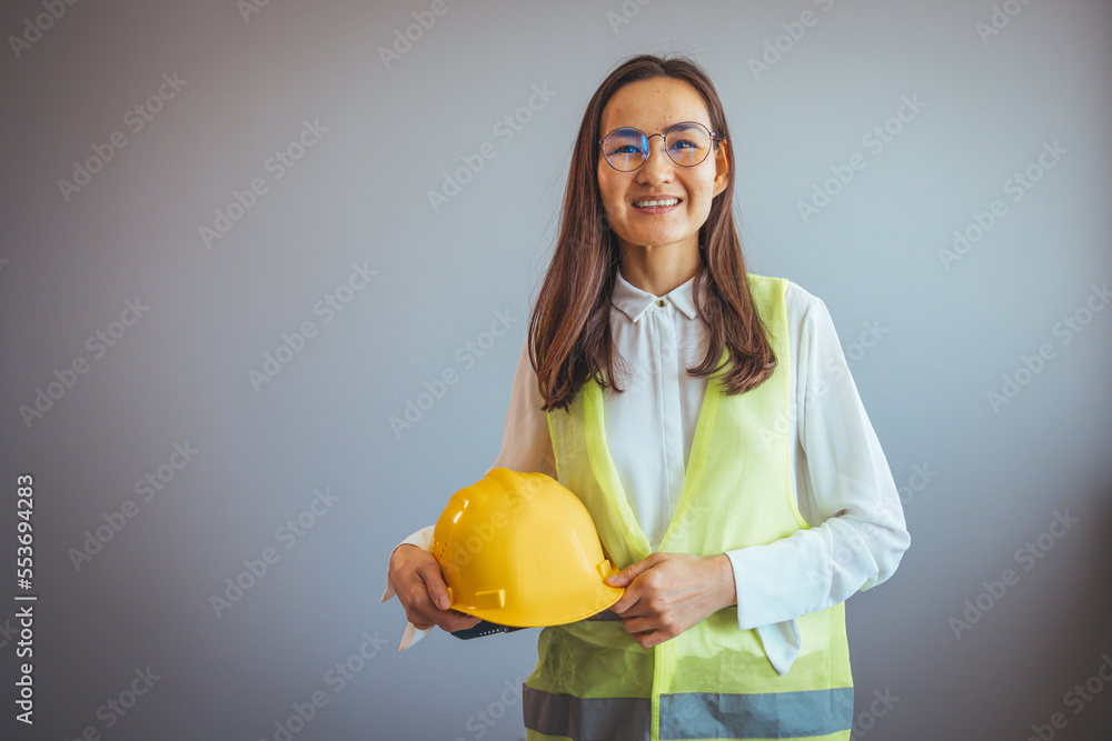 A portrait of a young female engineer looking at the camera on a construction site. Beautiful asian woman engineer and safety helmet on gray background, construction concept, Engineer, Industry. A portrait of a young female engineer looking at the camera on a construction site. Beautiful asian woman engineer and safety helmet on gray background, construction concept, Engineer, Industry.
