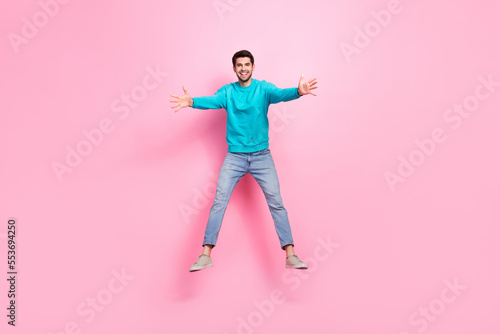 Full length photo of attractive young man jumping stretching hands hug excited dressed stylish blue look isolated on pink color background