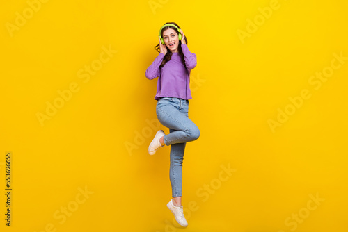 Full size photo of cheerful pretty girl hands touch headphones jumping isolated on yellow color background