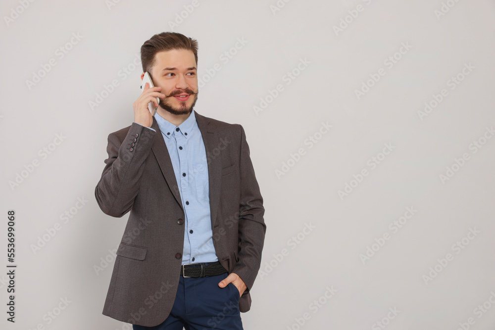 Happy man in suit talking on smartphone against light grey background. Space for text Happy man in suit talking on smartphone against light grey background. Space for text