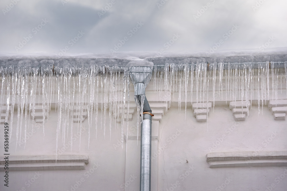 Icicles hanging down on drainpipe. Icicles on facade of building, dangerous sharp icicles on rooftop, risk of falling ice, danger for pedestrians. Icicles hanging down on drainpipe. Icicles on facade of building, dangerous sharp icicles on rooftop, risk of falling ice, danger for pedestrians.