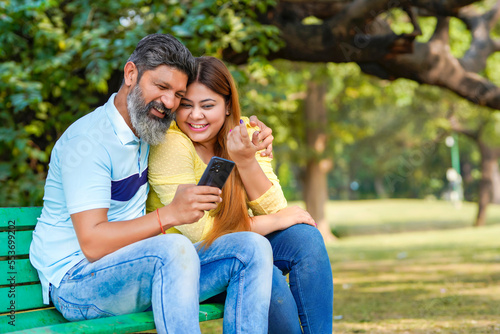 Indian man and woman watching some detail in smartphone at park. © Niks Ads