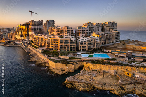 Skyline of Sliema, Malta at sunset. Blue sea waters and clear sky. Drone aerial view