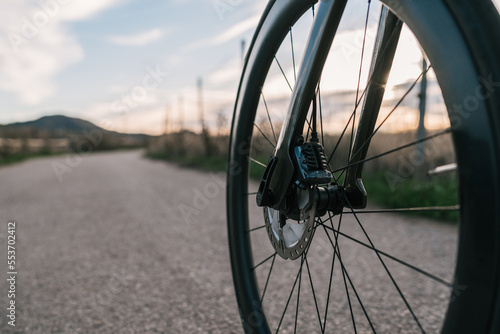 Wheel of a dark road bike on the asphalt at sunset.