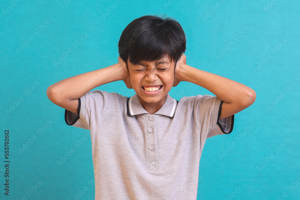 Displeased Asian boy covering his ears from the noise isolated on green background Displeased Asian boy covering his ears from the noise isolated on green background