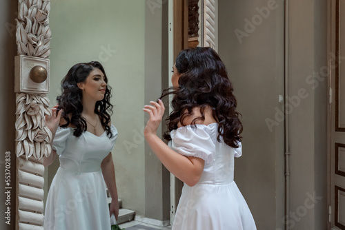 Bride in elegant dress looking in the mirror. Ukrainian bride preens at the mirror. Black-haired bride admiring herself in front of the mirror