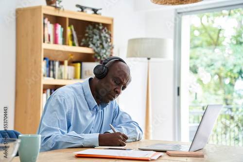 Mature African-American man wearing headphones while working at home with laptop computer