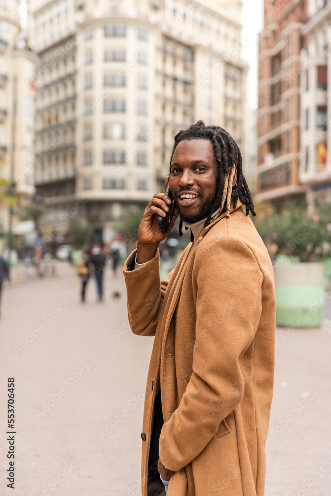 vertical picture of smiling african american man talking on the smartphone at the city looking at the camera vertical picture of smiling african american man talking on the smartphone at the city looking at the camera