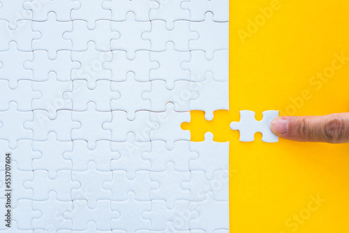 Hand putting the last piece of white jigsaw puzzle