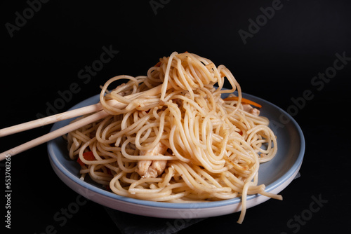 Japanese noodles with chicken and soy sauce on a blue plate on a black background. Dish of Asian cuisine