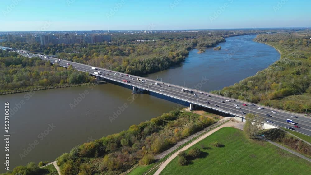 Aerial view of road bridge highway across the river in city area. Lorry is driving on the bridge. Sky reflections on the river water surface. Many cars Aerial view of road bridge highway across the river in city area. Lorry is driving on the bridge. Sky reflections on the river water surface. Many cars