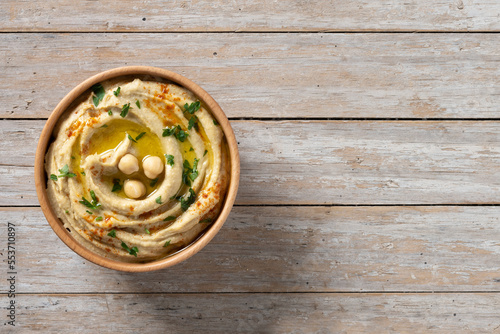 Chickpea hummus in a wooden bowl garnished with parsley, paprika and olive oil on wooden table. Top view. Copy space photo