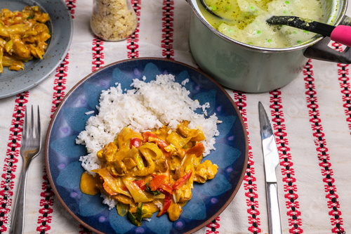 Homemade dining, luch or dinner. Asian food (turkey meat with vegetable and rice) on blue plate, pea soup in pot on table. photo