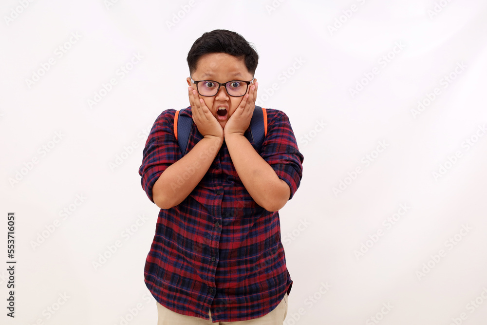 Cute asian school boy standing while showing shocked expression. Isolated on white background