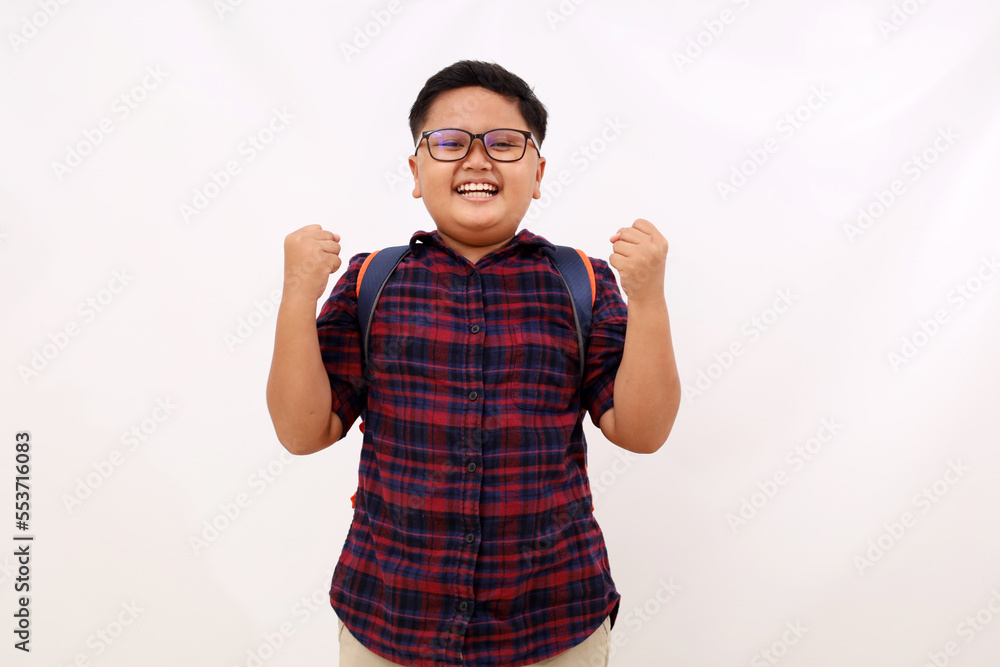Fototapeta premium Happy asian school boy with eyeglasses standing with clenched hand. Success concept. Isolated on white background