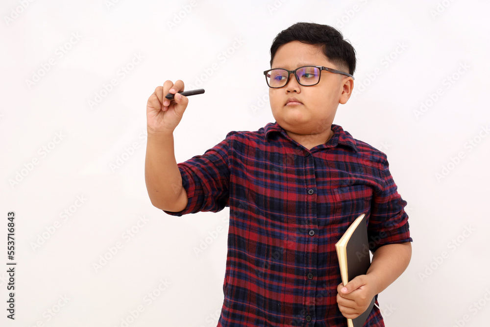 Asian school boy standing while writing something and carrying a book. Isolated on white background